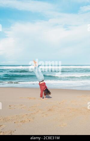 Young woman doing handstand at Ursa beach against sky, Portugal Stock Photo
