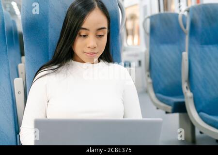Close-up of young woman using laptop while sitting on seat in train Stock Photo