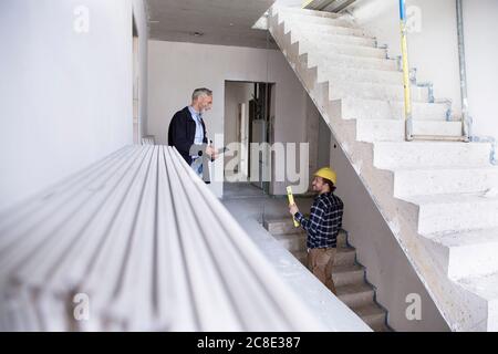 Architect and construction worker discussing while standing in constructing house Stock Photo