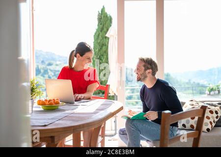 Happy mid adult couple sitting while looking at each other against window Stock Photo