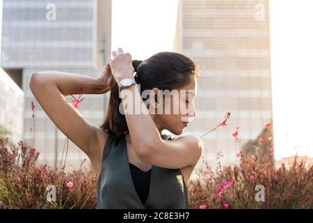 Close-up of woman with eyes closed tying hair against buildings in city Stock Photo