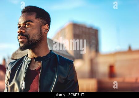 Close-up of thoughtful young man wearing leather jacket on rooftop in city Stock Photo