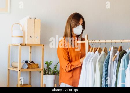 Female fashion designer working at home with clothes stand wearing protective face mask