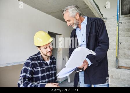 Architect and worker discussing building plan on a construction site Stock Photo