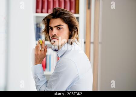 Thoughtful businessman holding pen looking away while sitting in office Stock Photo