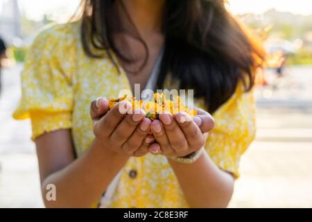 Young woman holding flowers in cupped hands in city during summer Stock Photo