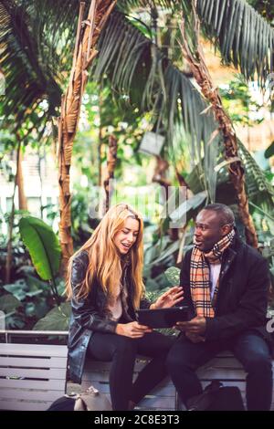 Business colleagues discussing over digital tablet while sitting on chairs against trees Stock Photo