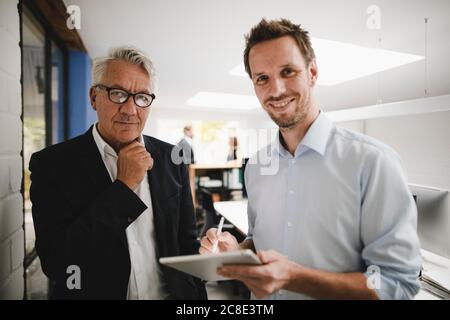 Two successful businessmen standing in office, using digital tablet Stock Photo