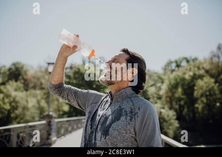 Tired mature man pouring water on face while standing against clear sky in park Stock Photo