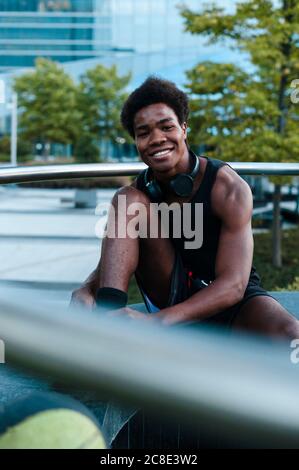 Portrait of a smiling young man with headphones sitting in the city Stock Photo