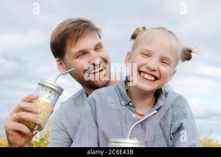 Smiling man and daughter enjoying lemonade against sky Stock Photo