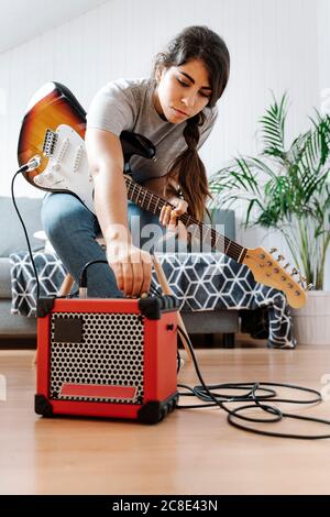 Woman adjusting knobs on amplifier while playing electric guitar at home Stock Photo