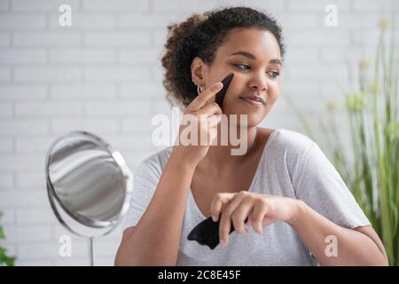 Close-up of young woman massaging face with gua sha stone at home Stock Photo