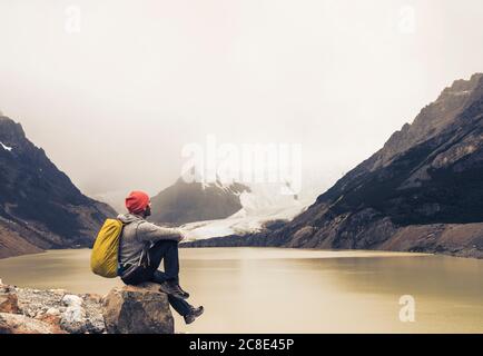 Man with backpack sitting on rock by lake at Patagonia, Argentina Stock Photo