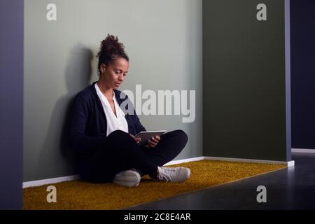 Portrait of businesswoman sitting on the floor in office using digital tablet Stock Photo