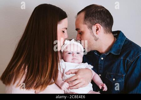 Parents kissing baby girl against wall at home Stock Photo