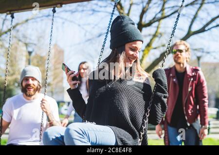 Happy young woman swinging while enjoying with friends in park Stock Photo