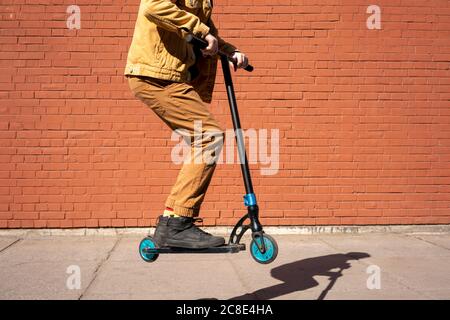 Boy performing stunt on with push scooter at sidewalk against brick wall Stock Photo