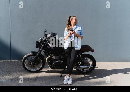 Smiling woman sitting on motorbike and using smartphone Stock Photo
