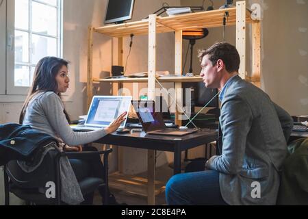 Businessman and woman using laptops at desk in office Stock Photo