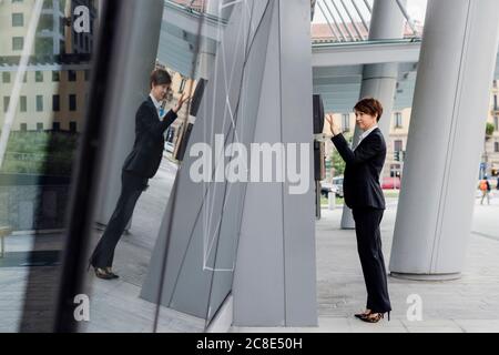 Businesswoman with short hair using ATM while reflection on modern building in city Stock Photo