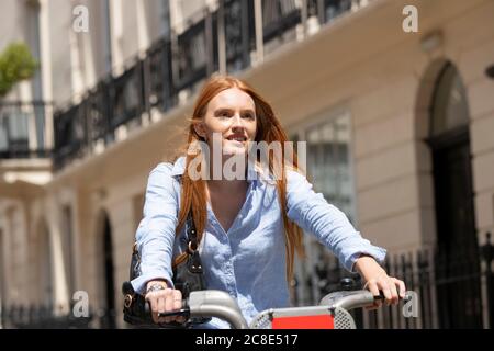 Beautiful woman riding hire bike in city during sunny day Stock Photo