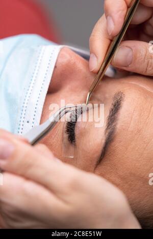 Hands of beautician using tweezers on customer for eyelash extension at beauty spa Stock Photo