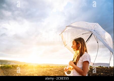 Girl holding umbrella while looking away during sunset Stock Photo