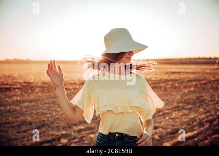 Young woman tossing hair on field against sky during sunset Stock Photo