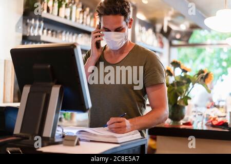 Restaurant manager with protective mask using computer and smartphone for reservation Stock Photo
