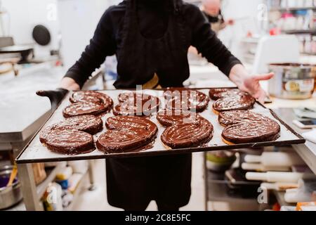 Female baker holding heart shaped dessert in baking tray at bakery Stock Photo