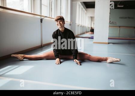 Happy ballet dancer stretching legs on floor in dance studio Stock Photo