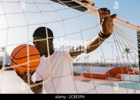 Young man kissing basketball while standing by net in court during sunny day