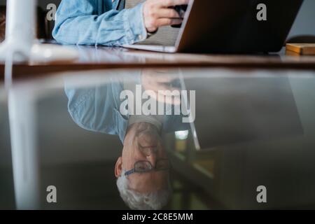 Reflection of senior man using laptop and smart phone in table at home Stock Photo