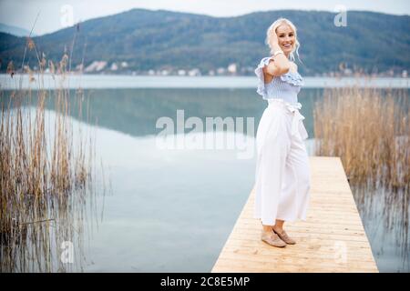 Portrait of fashionable blond woman standing on jetty at Woerthersee, Austria Stock Photo