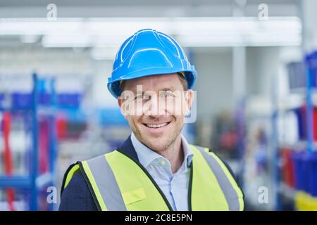 Happy male supervisor wearing hardhat and reflective clothing in factory Stock Photo
