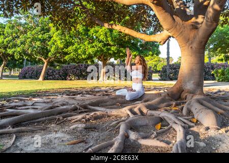 Mature woman mediating while sitting on roots in park Stock Photo