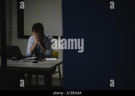 Exhausted businessman covering face, sitting in office, working late Stock Photo