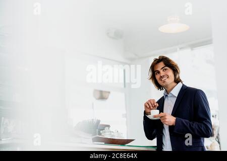 Smiling male entrepreneur looking away while holding coffee cup in cafe Stock Photo