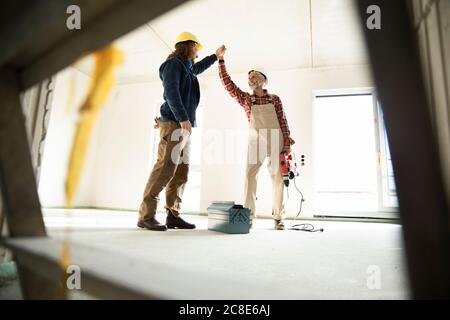 Male coworkers giving high five while standing in renovating house Stock Photo