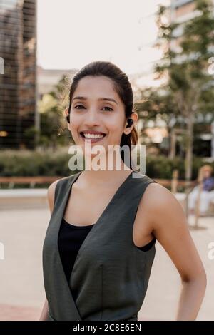 Close-up of smiling female entrepreneur wearing wireless earphones Stock Photo