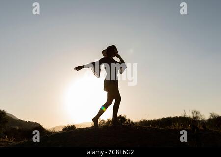Young woman standing on hill at countryside against clear sky Stock Photo