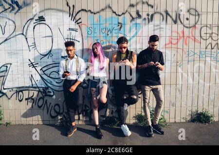 Group of friends using smartphones at a graffiti wall in the city Stock Photo