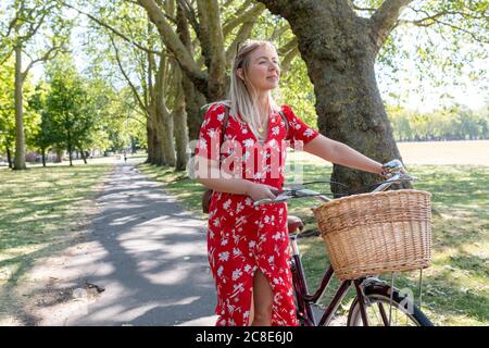 Beautiful woman walking with bicycle on footpath in public park Stock Photo