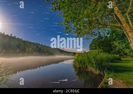 Idyllic night scenery under the star trailed night sky at a lake with reflection of the stars. Stock Photo