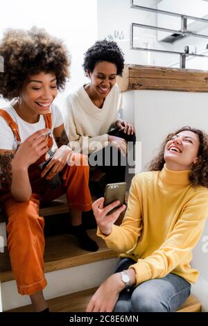 Three laughing young women having fun with smartphone at home Stock Photo