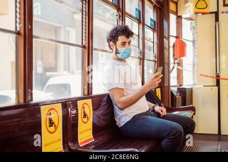 Young man wearing face mask using smart phone while sitting in tram Stock Photo