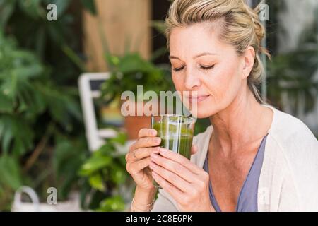 Portrait of mature woman with eyes closed with glass of green smoothie Stock Photo