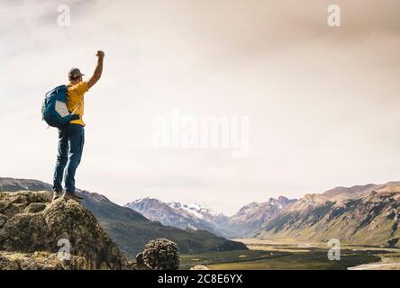 Man with arm raised looking at mountains while standing on rock, Patagonia, Argentina Stock Photo