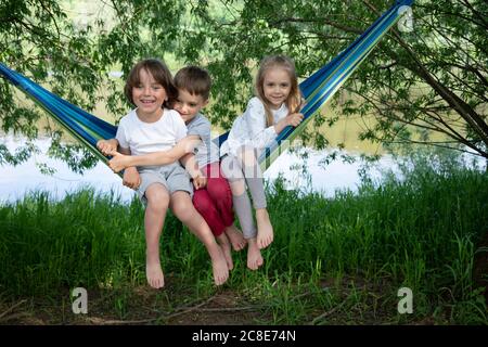 Cheerful friends sitting on hammock in forest Stock Photo